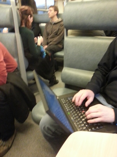 People in train working on computer and knitting